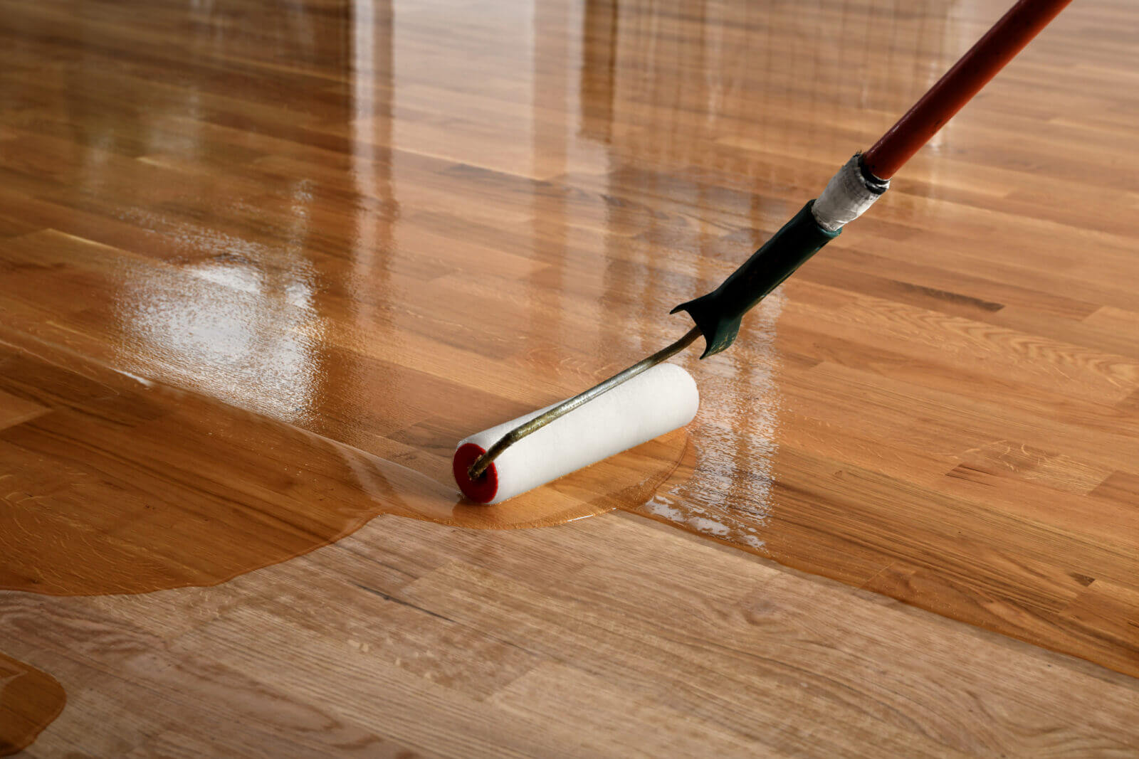 stufex - Lacquering wood floors. Worker uses a roller to coating floors.